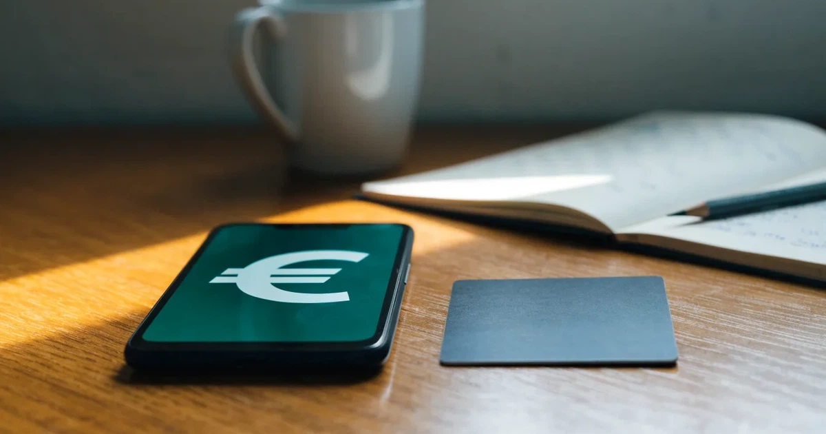 Uno smartphone e una carta di pagamento affiancati su un tavolo di legno, con alcune banconote da euro accanto
