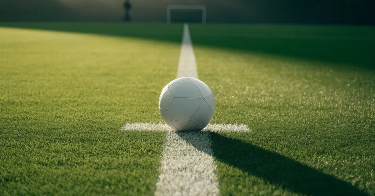 Un pallone da calcio sul dischetto del centrocampo di un prato, alla luce del mattino